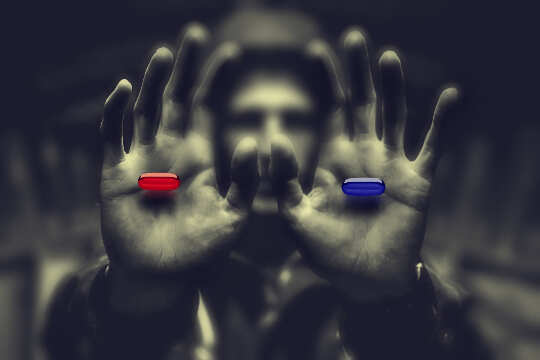 mann i skygger som holder frem en rød pille i den ene hånden og en blå pille i den andre