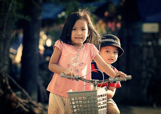 gadis muda di atas sepeda dengan saudara laki-lakinya duduk di belakangnya