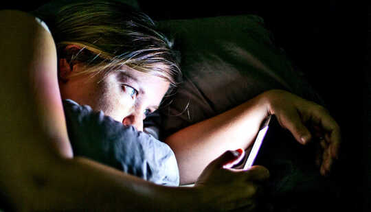 बिस्तर में एक महिला अपना फोन पढ़ती है