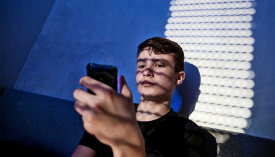 Un muchacho adolescente se sienta en la cama leyendo su teléfono