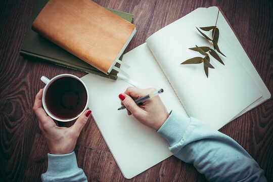 person, der skriver i en notesbog, der holder en kop kaffe
