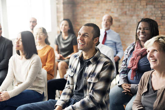 Un grupo de adultos en un salón de clases, sonriendo a la maestra que está fuera del marco.