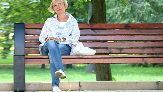 زنی خندان که روی یک نیمکت عمومی نشسته است