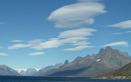 Lenticular clouds form over mountains.