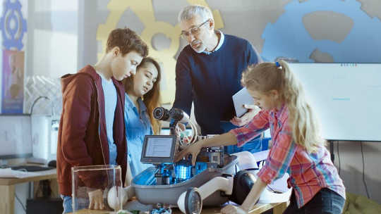शिक्षक और छात्र एक विज्ञान परियोजना के लिए एलईडी रोशनी के साथ एक प्रोग्राम करने योग्य रोबोट पर काम करते हैं। (पूछताछ आधारित सीखने से आपके बच्चे को क्यों फायदा होगा)