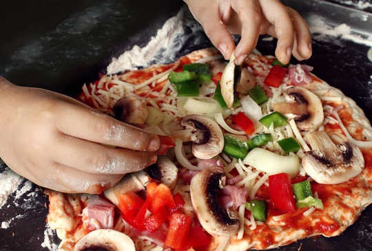Gitt muligheten, barn er stolte av å lage sin egen pizza og bidra til middag. (hvordan å øke barnaferdigheter og minner med en ukentlig spillnatt)