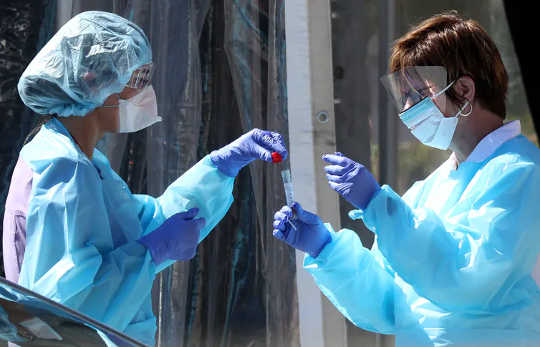 Medisch personeel beveiligt een monster van een persoon bij een drive-through coronavirus COVID-19-teststation