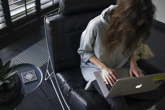 Seorang wanita dengan hoodie membungkuk di atas laptopnya.