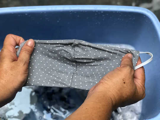 Una persona que se lava la máscara en un balde con agua y detergente