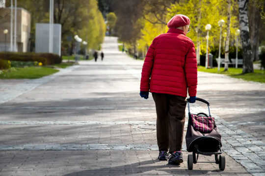 Donna anziana che cammina con la borsa della spesa di rotolamento.