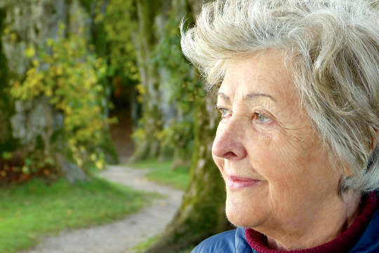 een oudere vrouw die buiten staat te kijken naar iets in de verte