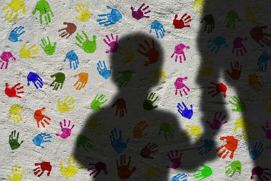 Silhouette d'un garçon tenant la main d'un adulte, avec un fond d'empreintes de mains colorées sur le mur