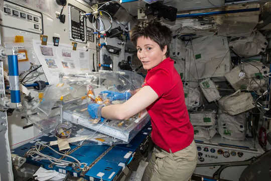 Wanita dalam gravitasi nol melakukan eksperimen, dikelilingi peralatan.