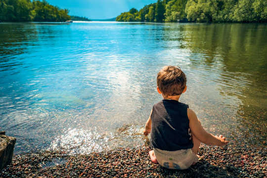 jeune enfant assis au bord d'un lac paisible