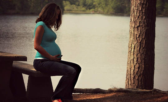 그녀의 배꼽에 그녀의 손으로 앉아 임신한 여자