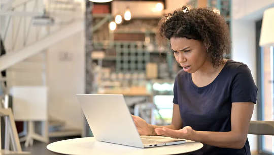 Mujer molesta sentada frente a su computadora portátil abierta