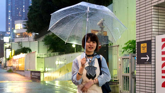 Jovem sorridente caminhando com o guarda-chuva aberto
