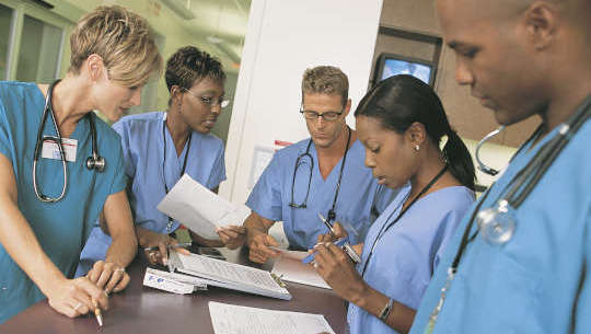 grupa pracowników służby zdrowia stojących wokół biurka lub stołu