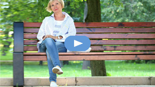 mosolygós nő ül egy nyilvános padon