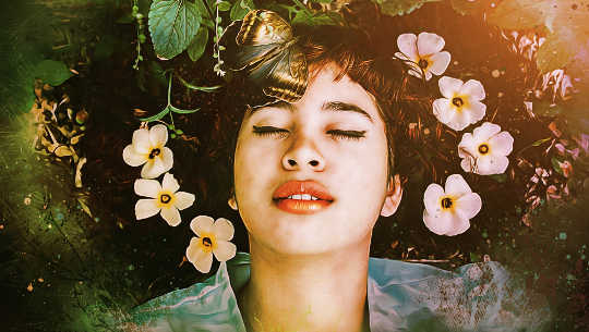 uma mulher deitada na natureza com os olhos fechados e flores no cabelo