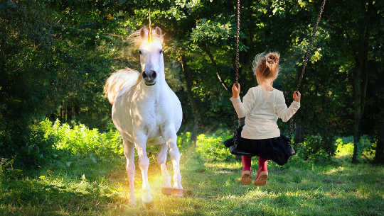 niña joven en un columpio mirando un unicornio