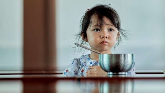 کودک ناراضی که جلوی ظرف غذا نشسته است