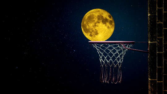 a full moon just over the edge of a basketball hoop