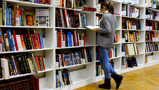 flicka som står och tittar på en bok framför hyllor i en bokhandel