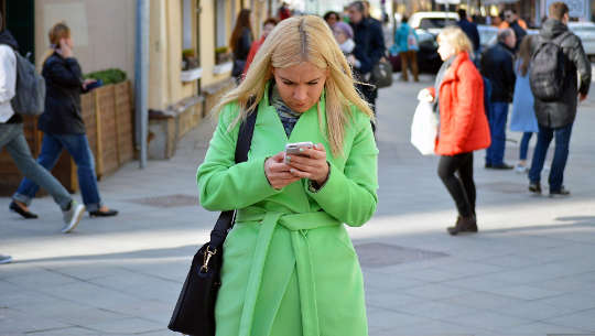 wanita di jalan menatap ponselnya dengan penuh perhatian