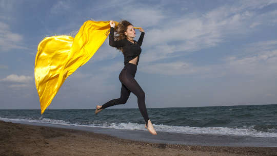 彼女の後ろの風に飛んでいる岬と一緒にビーチを走っている女性
