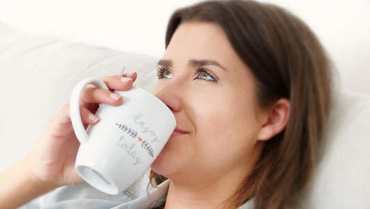 femme buvant dans une tasse avec un regard satisfait sur son visage