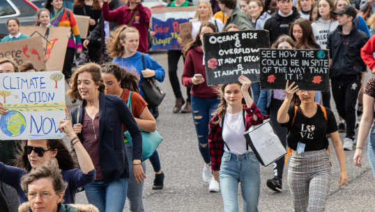 folla di persone che marciano con segni del cambiamento climatico e altro