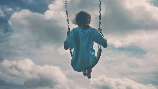 person sitting on a swing way up in the sky facing clouds