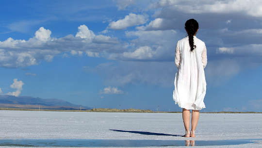 فتاة تقف حافية القدمين على الشاطئ وتطل على ما وراء البحار
