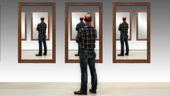 mężczyzna zatrzymał się, by spojrzeć na swoje odbicie w trzech oddzielnych lustrach