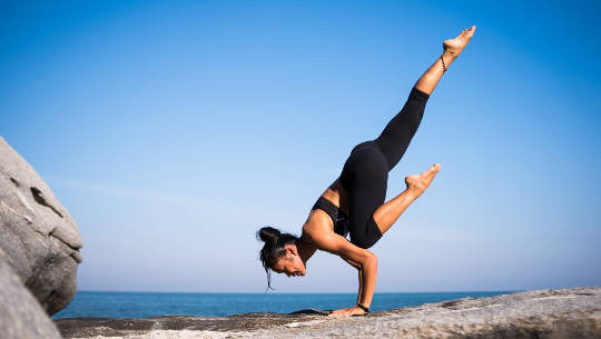 女人在她的手上保持平衡，在海滩上做瑜伽姿势