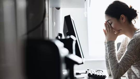 egy nő a számítógép előtt, kezével eltakarja az arcát