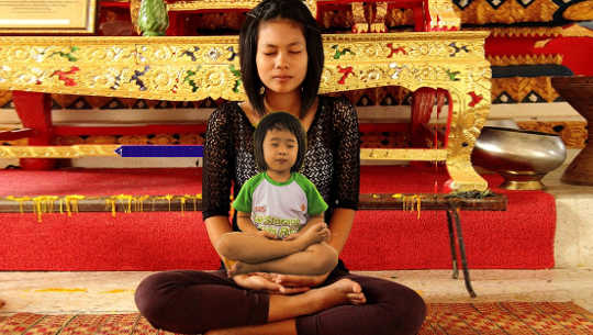 seorang wanita dalam posisi lotus dengan seorang anak, mungkin anak batinnya, di pangkuannya juga dalam posisi lotus