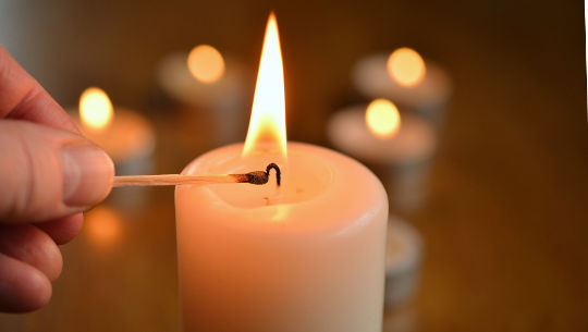 dłoń zapalająca świeczkę, z innymi zapalonymi świecami w tle