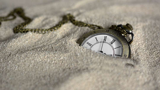 um relógio de bolso semi-enterrado na areia