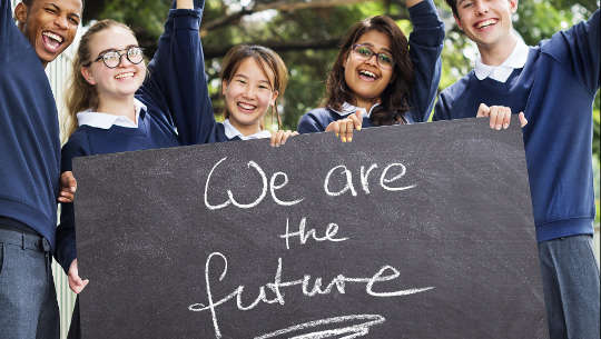 「私たちは未来です」と書かれた看板を掲げている小学生