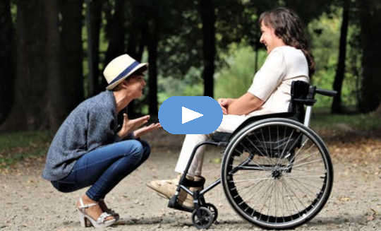 περιποιητικό άτομο που κάθεται οκλαδόν μπροστά σε άλλον σε αναπηρικό καροτσάκι
