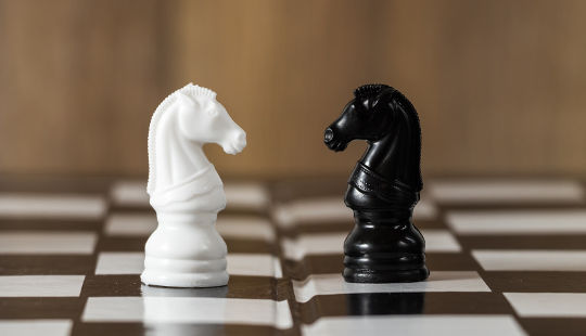 duas peças de xadrez, um cavalo branco e um cavalo preto, um de frente para o outro em um tabuleiro de xadrez