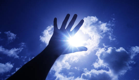 åben hånd løftet op mod solen og himlen