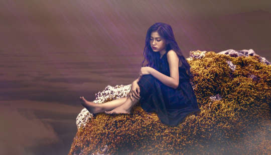Töprengő fiatal lány ül egy sziklán