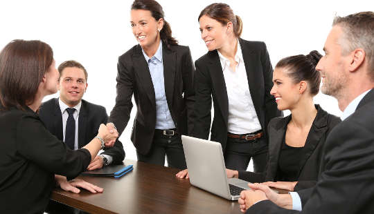 donne che si stringono la mano a una riunione di lavoro, con uomini che guardano