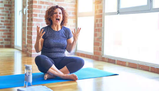 femme assise sur un tapis de yoga avec les mains en l'air de frustration et de cris