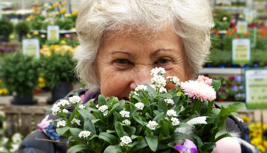 foto de uma mulher mais velha com cabelos brancos atrás de um buquê de flores