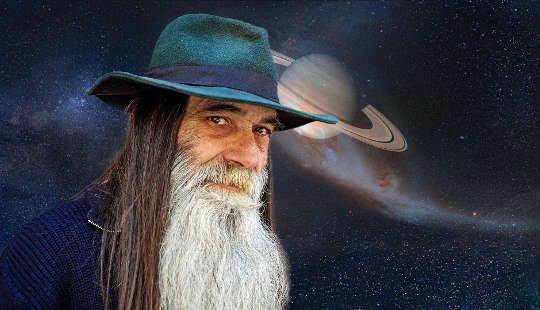ستاروں سے بھرے آسمان اور سیارے کے سامنے کھڑا لمبی داڑھی والا بوڑھا آدمی