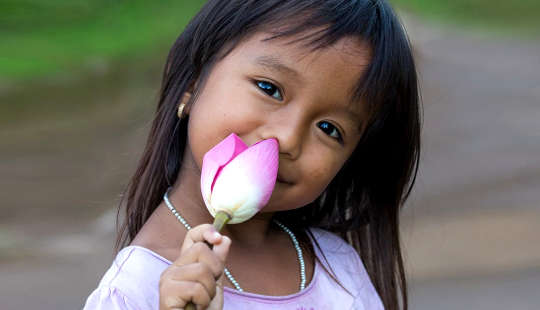 دختر جوان خندان که یک گل نیلوفر باز نشده در دست دارد